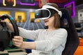 Teenage girl wearing virtual reality glasses, who holds on to the steering wheel and plays a computer game on the Royalty Free Stock Photo