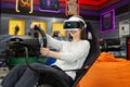 Teenage girl wearing virtual reality glasses, who holds on to the steering wheel and plays a computer game on the Royalty Free Stock Photo