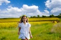 Teenage girl in white dress and Ukrainian wreath runs through yellow fields and green meadows, against cloudy sky Royalty Free Stock Photo