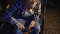 Teenage girl whittling twig with knife in forest camp at night