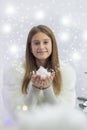 teenage girl in winter clothes, a white fur coat, holds artificial snow, demonstrates to the camera, smiles, against the backdrop Royalty Free Stock Photo