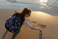 A teenage girl writes on the sand in the beach Royalty Free Stock Photo