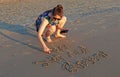 A teenage girl writes on the sand in the beach Royalty Free Stock Photo