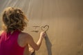 teenage girl writes on the sand I love while sitting on the sea coast Royalty Free Stock Photo