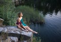 teenage girl and a boy, brother and sister, are happily sitting together on rock near lake and fantasize with interes Royalty Free Stock Photo