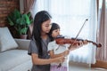 Teenage girls help a child hold the violin bow properly while playing the violin indoors