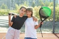 Teenage girls with racquets and balls standing in padel court, looking at camera and smiling. Royalty Free Stock Photo