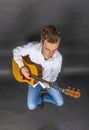 Teenage guitar player sits on a chair and plays western guitar Royalty Free Stock Photo