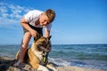 Teenage guy with blond hair and leash in hands plays and walks with dog of Akina Inu breed on wild beach along Black Sea Royalty Free Stock Photo