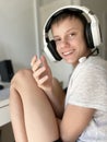 A teenage guy smiles sincerely while sitting at a computer in white headphones