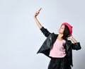 Teenage kid in black leather jacket, skirt and pink hat. She taking selfie using smartphone, posing isolated on white. Close up Royalty Free Stock Photo