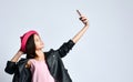 Teenage kid in black leather jacket, skirt and pink hat. She taking selfie using smartphone, posing isolated on white. Close up Royalty Free Stock Photo