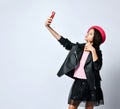 Teenage kid in black leather jacket, skirt and pink hat. She taking selfie using smartphone, posing isolated on white. Close up Royalty Free Stock Photo