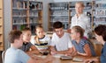 Teenage pupils sitting at table and studying, teacher in classroom