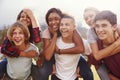 Teenage school friends having fun piggybacking outdoors