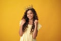 Teenage selfish girl celebrates success victory. Teen child in queen crown isolated on yellow background. Princess in