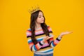 Teenage selfish girl celebrates success victory. Teen child in queen crown on yellow background. Princess girl