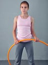 Teenage sportive girl is doing exercises with hula hoop to develop muscle on grey background. Having fun playing game hula-hoop.
