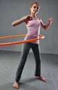 Teenage sportive girl is doing exercises with hula hoop to develop muscle on grey background. Having fun playing game . Sport heal