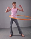 Teenage sportive girl is doing exercises with hula hoop to develop muscle on grey background. Having fun playing game . Sport heal