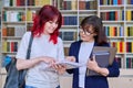 Teenage student girl talking to female teacher mentor in the library. Royalty Free Stock Photo