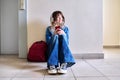 Teenage student in headphones with backpack smartphone sitting on floor near wall. Royalty Free Stock Photo