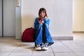 Teenage student in headphones with backpack smartphone sitting on floor near wall. Royalty Free Stock Photo