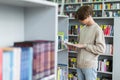 teenage student reading book near bookshelves