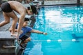 teenage swimmer standing on block board and preparing to jump and swim with a coach giving instructions