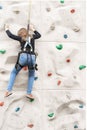 Teenage teen girl grabbing artificial high climbing wall with split ledges. Climbing harness safety sports equipment Royalty Free Stock Photo