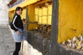A teenage Tibetan girl stands before golden prayer wheels.