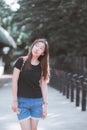 Teenage woman makes a funny face and stands smiling on the street. People wear casual clothes in a black T-shirt and shorts.