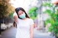 Teenage women walking on the street. She wears a green medical face mask and is scratching her head. Face shows confusion.