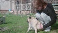 Teenaged blond girl pets cute pugdog. Side view.