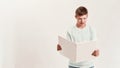 Teenaged disabled boy with Down syndrome looking focused while reading a book, standing isolated over white background Royalty Free Stock Photo