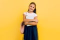 A teenager with a backpack and books. Stylish beautiful schoolgirl posing on a yellow background