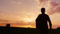 A teenager with a backpack over his shoulder goes towards the sunset in the field or in the countryside. Concept - new