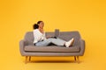 teenager black girl uses laptop on sofa against yellow background