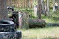 A teenager in a black protective mask and camouflage clothes with arms in his hands hides behind iron barrels and tires. Landfill