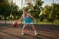 Teenager boy dribbling ball playing street basketball on city court