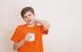 Teenager boy drinking a cup of coffee over white background. Sleepy teen in orange t-shirt with coffee mug yarning