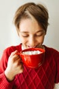 Teenager boy drinks cocoa with marshmallows from a red cup. Soft selective focus.