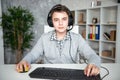 A teenager boy in headphones playing computer games at pc at home in the interior in front of a computer monitor Royalty Free Stock Photo