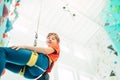 Teenager boy at indoor climbing wall hall. Boy is climbing using a top rope and climbing harness and somebody belaying him from fl Royalty Free Stock Photo