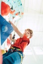 Teenager boy at indoor climbing wall hall. Boy is climbing using a top rope and climbing harness and somebody belaying him from fl