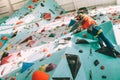 Teenager boy at indoor climbing wall hall. Boy is climbing using a top rope and climbing harness and somebody belaying him from