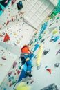 Teenager boy at indoor climbing wall hall. Boy is climbing using a top rope and climbing harness and somebody belaying him from