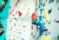 Teenager boy at indoor climbing wall hall. Boy is climbing using a top rope and climbing harness and somebody belaying him from