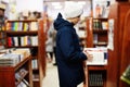 Teenager boy in jacket reaching a book from bookshelf at the library. Learning and education of european kid Royalty Free Stock Photo