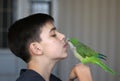 Teenager boy is playing with his green quaker parrot